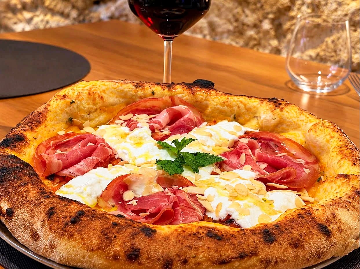 La Cortile Cascino da vicino: cornicione alto e maculato, crema di zucca, stracciatella, rose di pancetta coppata, mandorle a scaglie e un rametto di menta, sul tavolo di rovere con un calice di rosso.