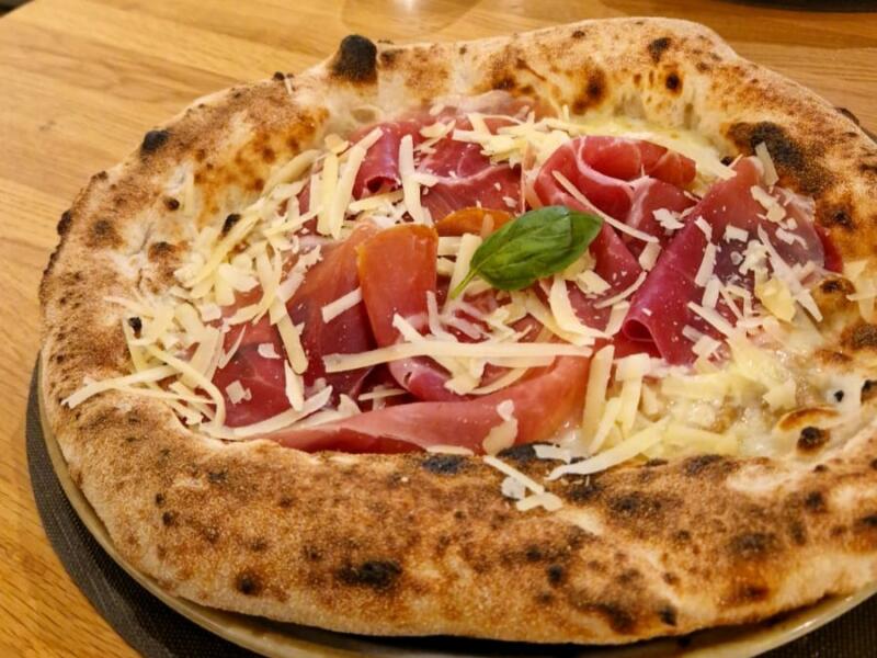 Pizza bianca con prosciutto crudo e scaglie di formaggio stagionato, cornicione alto e maculato dalla cottura.