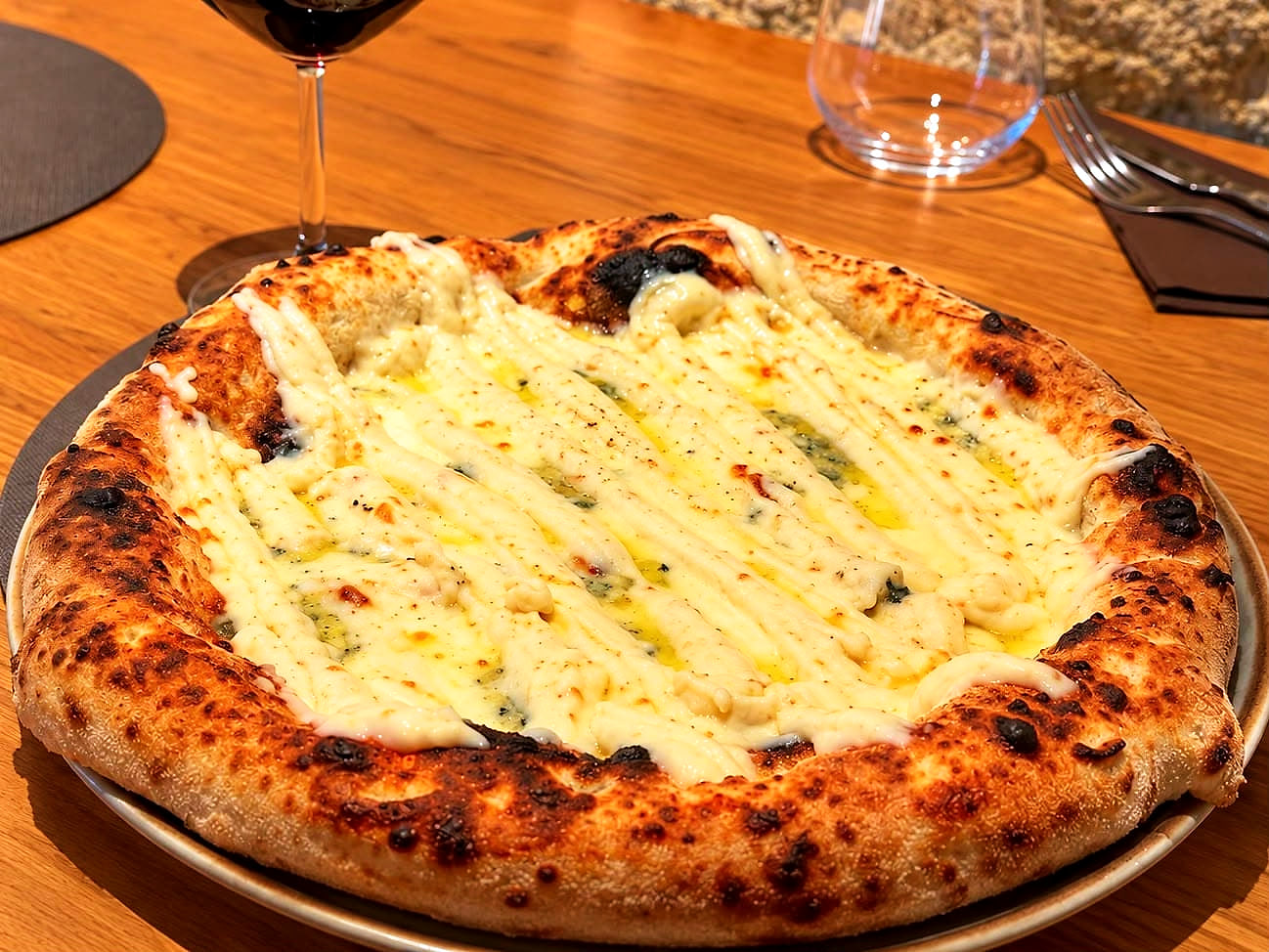 La Formaggi, bianca: strisce di fonduta di scamorza affumicata sul fiordilatte, con il caciocavallo e le chiazze di gorgonzola, su un cornicione alto e maculato dalla cottura, davanti al muro di tufo.