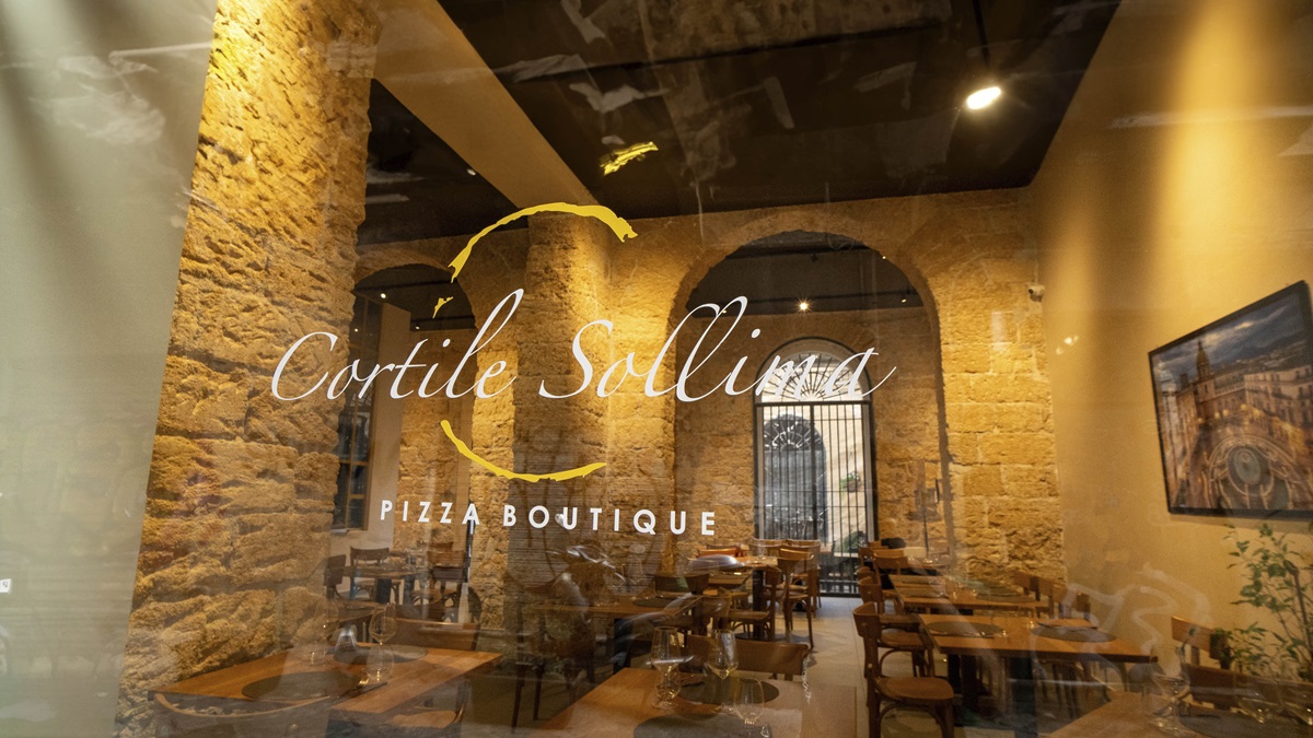 L'ingresso da via Calascibetta: il nome del locale sulla vetrata, con le arcate di tufo illuminate dietro il vetro.
